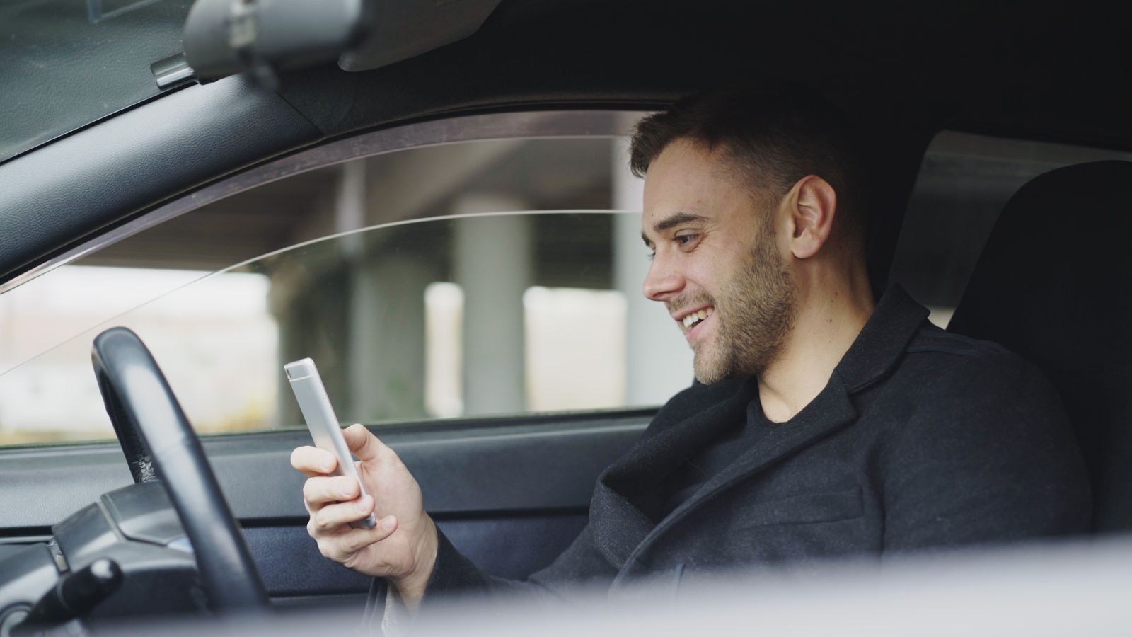 Chauffeur souriant consultant son téléphone dans sa voiture